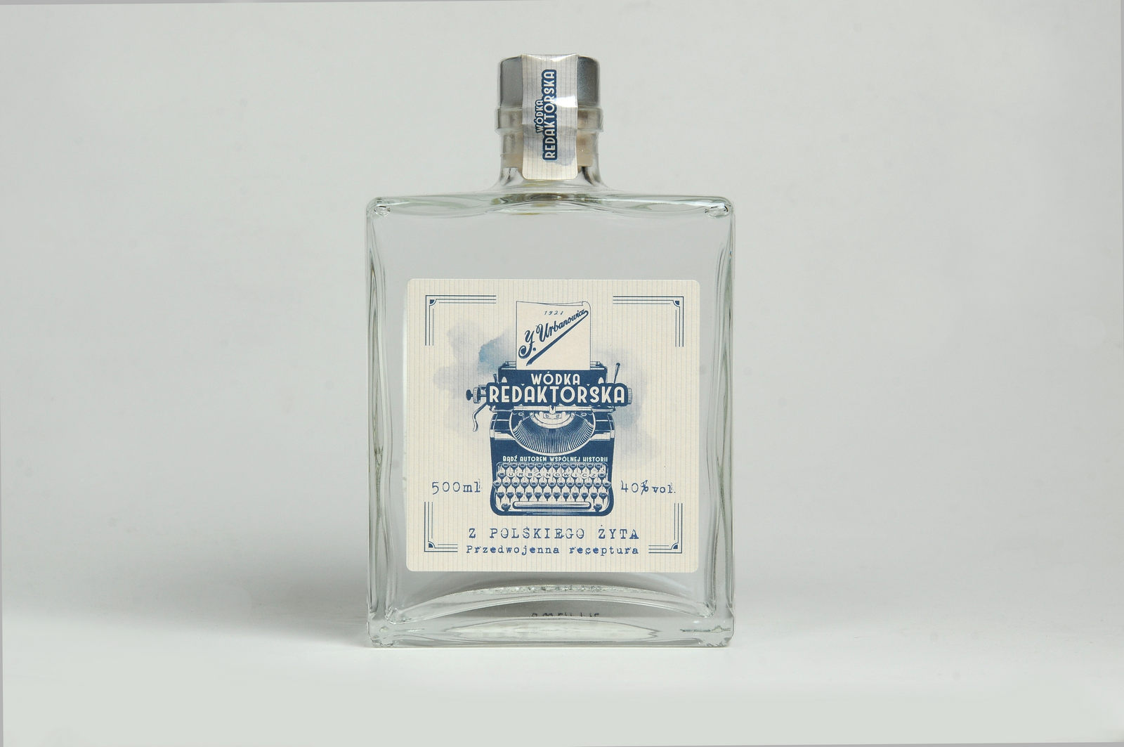 Kwadratowa duża butelka z wódką żytnią Redaktorską z ładną etykietą. Butelka stoi na białym tle.