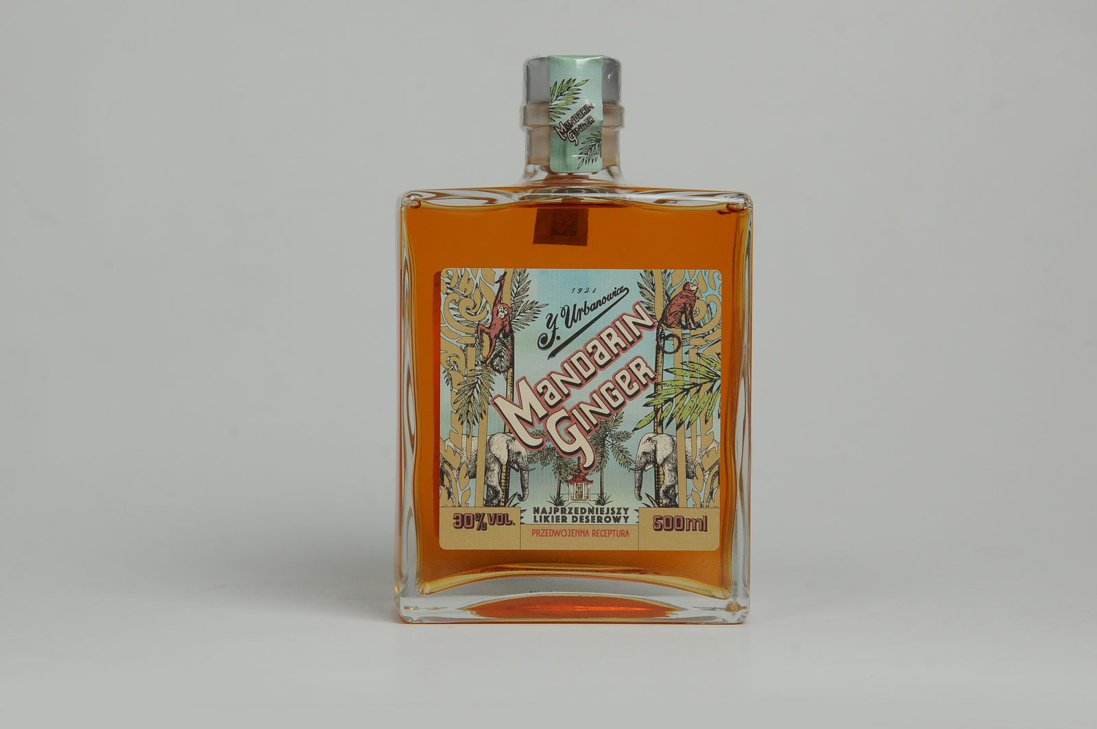 Likier owocowy Mandarin Ginger w kwadratowej, dużej butelce. Kolorowa etykieta. Butelka stoi na białym tle.
